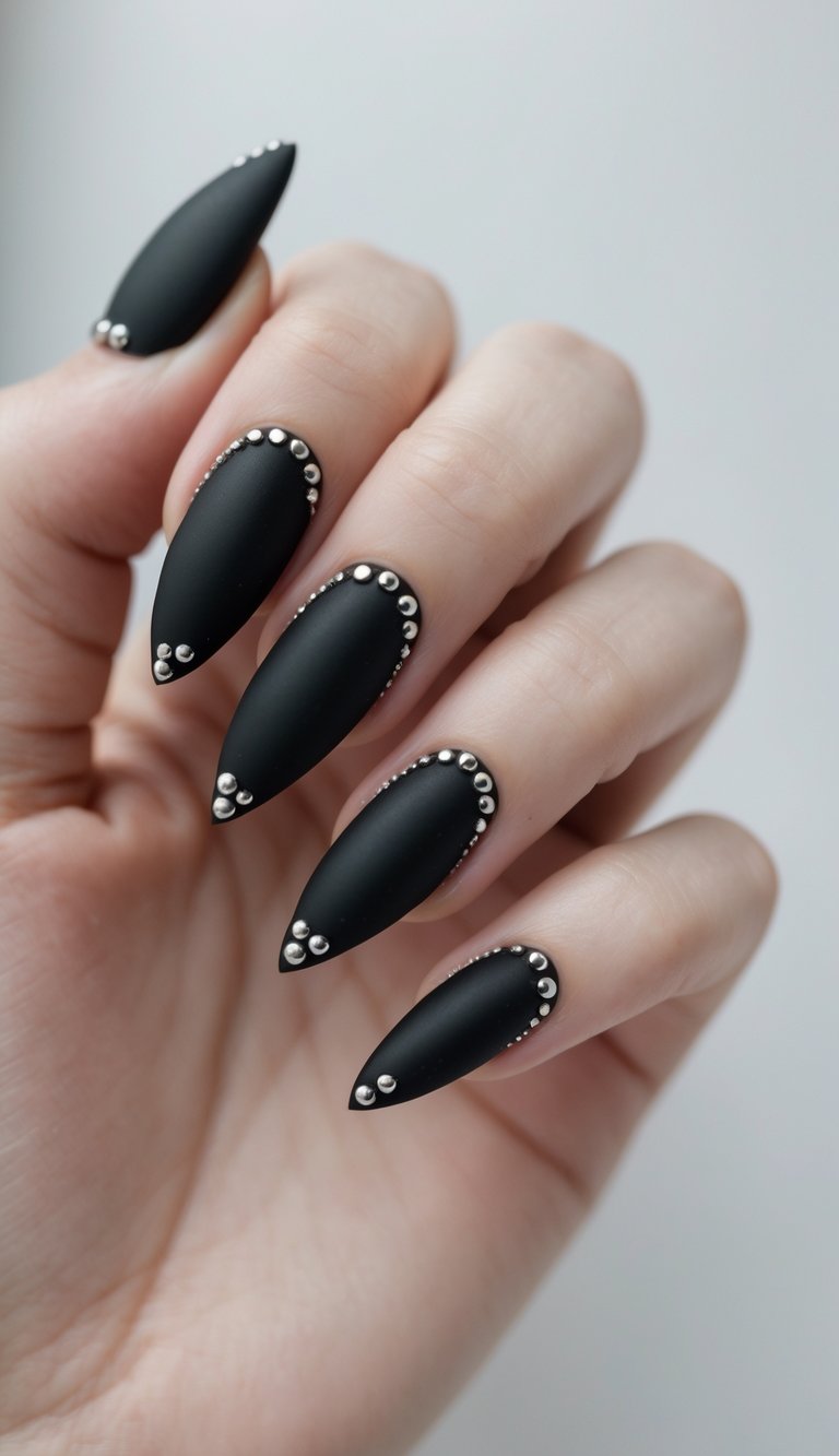 Stiletto nail art idea featuring matte black pointed nails decorated with silver studs along the edges