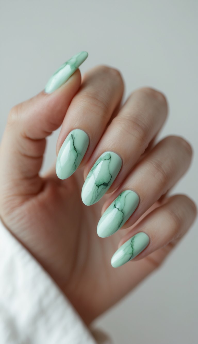 Fingertips shown with mint green round nails, detailed with fluid, dark green marble streaks that create a textured stone-inspired effect under a shiny finish.