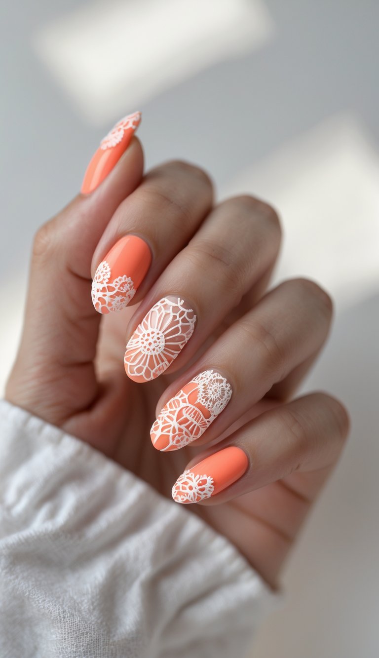 A hand with almond-shaped coral nails featuring detailed white floral lace accents, giving the illusion of embroidered patterns over a vibrant, peach-toned base.