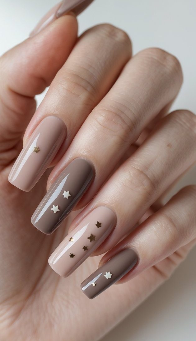 Square nail art idea shown on a hand featuring glossy beige and mocha-toned nails, each embellished with small metallic and white star-shaped stickers.