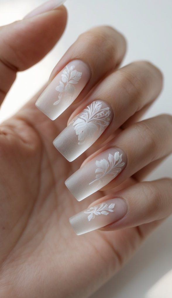 A hand featuring a square nail art idea with matte sheer-white nails, each accented by fine embossed floral designs for a romantic, airy finish.