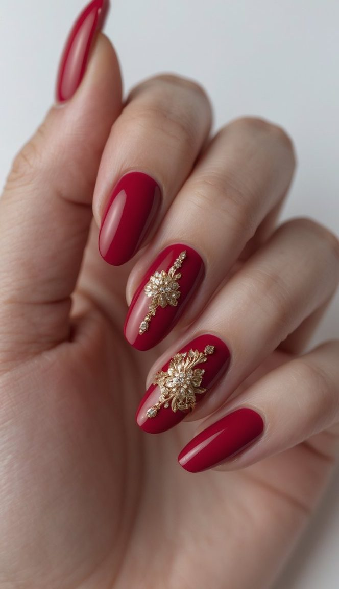 Close-up of a hand featuring a classy anniversary nail art idea with cranberry-red nails and gold floral designs adorned with crystals on the middle and ring fingers.
