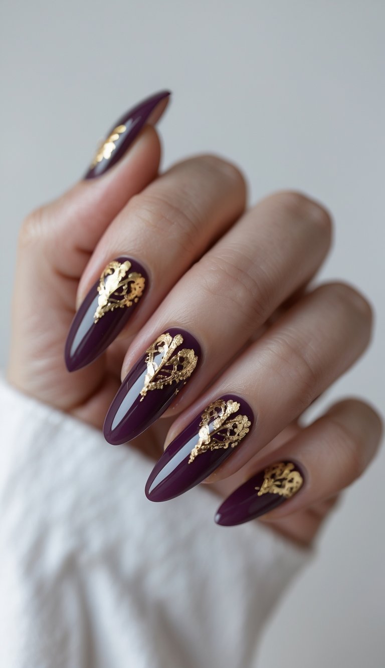 Close-up of a bold anniversary nail art idea with deep wine nails and gold foil art resembling ornate, artistic detailing across each long almond-shaped nail.