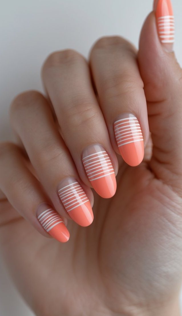 Trendy anniversary nail art idea shown on a hand with soft coral tips and minimal horizontal white striping, offering a clean and modern aesthetic.