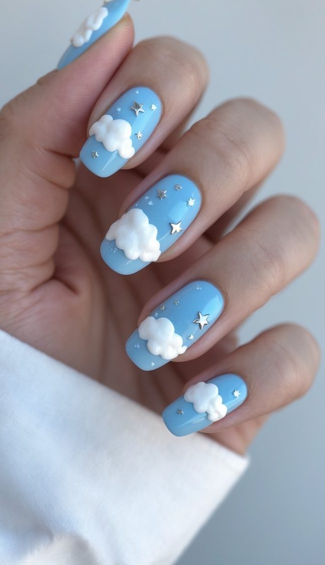 Shown in soft lighting, rounded blue nails with cloud embellishments and metallic star details highlight a whimsical graduation nail art idea.