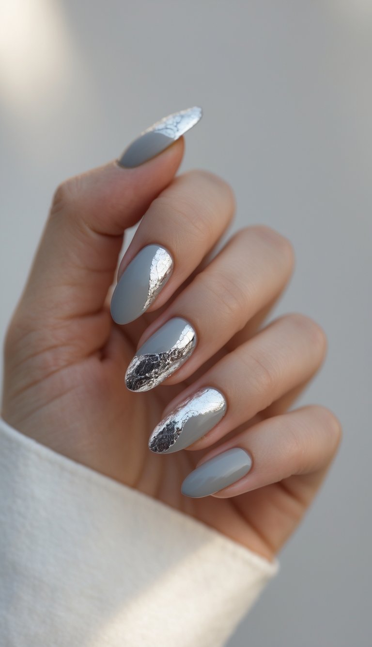 A hand with matte gray nails layered in silver foil that looks fluid and reflective, offering a creative engagement nail art idea with bold contrasts.