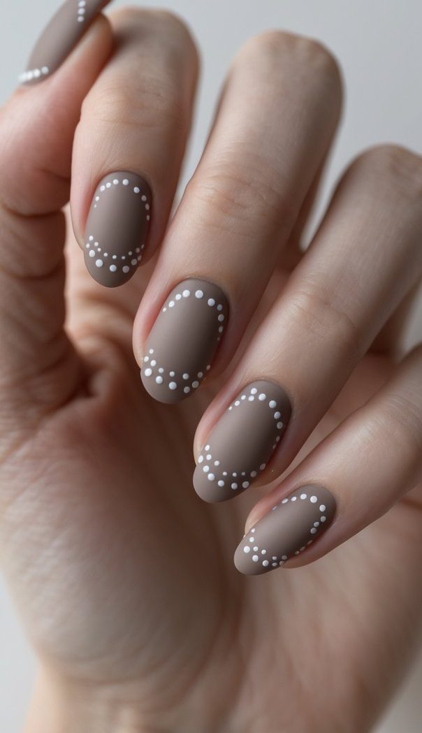 Close-up of taupe matte nails with dainty dotted white accents along the edges, offering a soft and stylish engagement nail art idea for the modern minimalist.