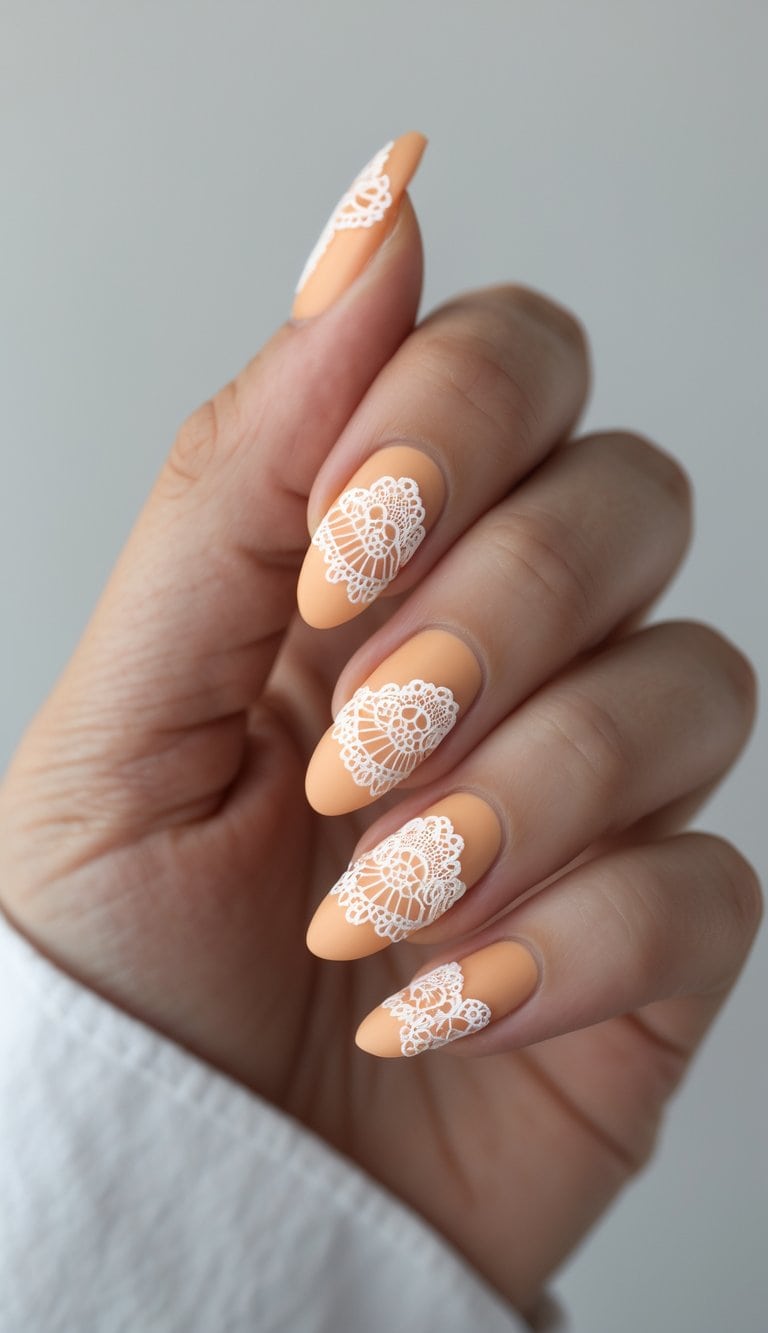 Close-up of hands with almond peach nails decorated in white lace accents, presenting romantic and sophisticated march nail art ideas.