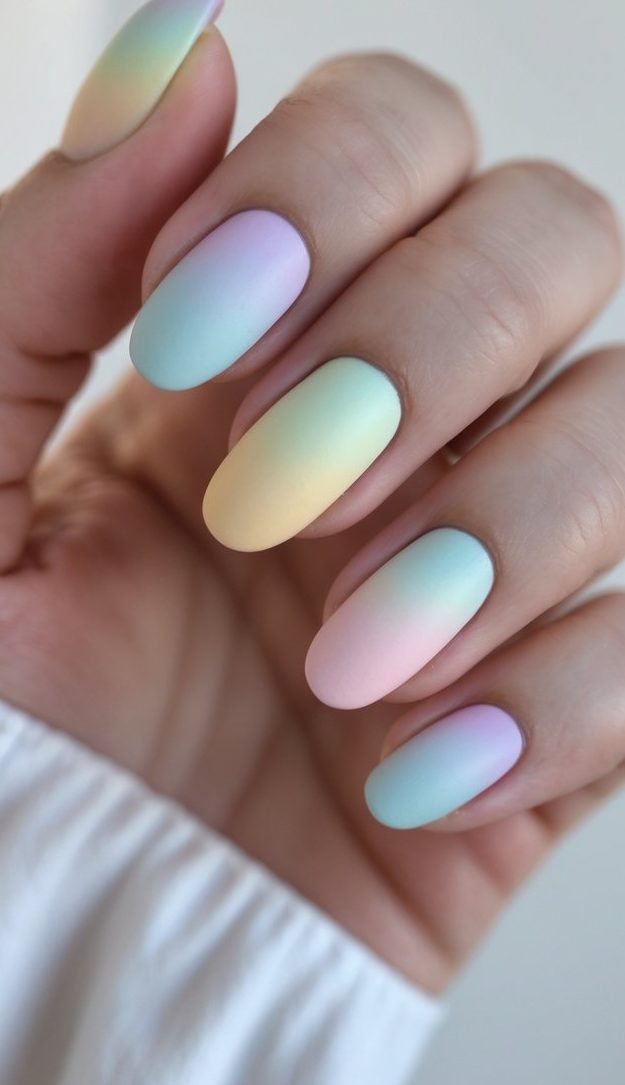A softly lit hand with rounded pastel nails, each one shifting from pink to mint to lilac in a seamless gradient that gives spring a modern, relaxed twist.