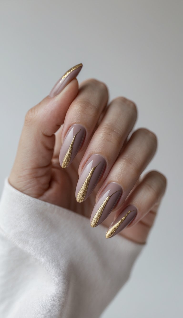 Close-up of hands with glossy mauve almond nails featuring gold foil accents, showing an elegant twist on march nail art ideas.