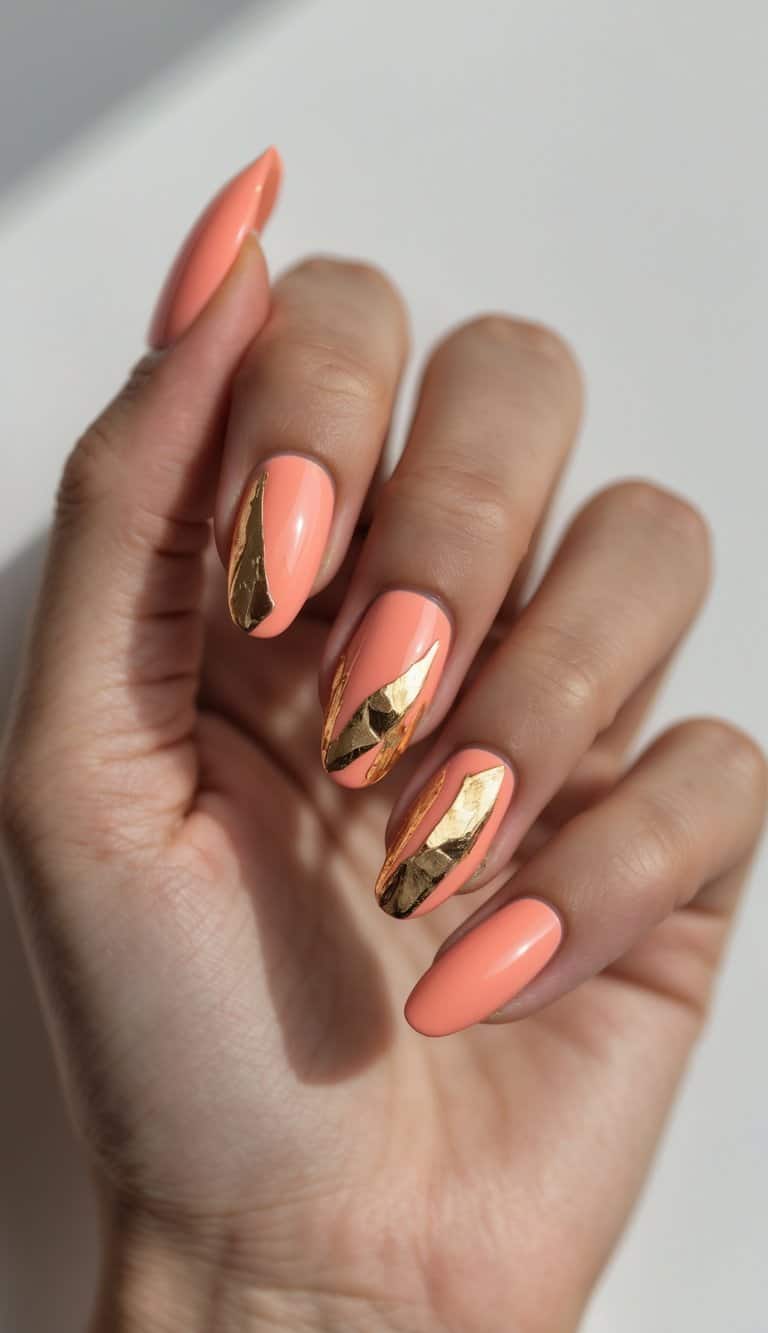 Close-up of hands with coral-orange nails and abstract gold foil tips, capturing bold elegance in luxe march nail art ideas.