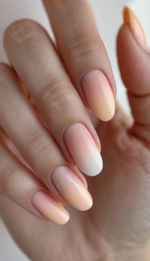 Hand displaying almond-shaped nails with blended pastel peach and cream hues, finished with a soft-glitter accent for a refined, summery design.