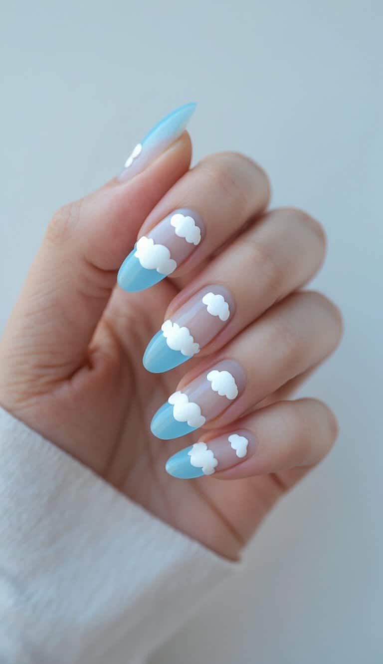 A close-up of a hand shows almond-shaped nails with blue tips and white cloud designs layered over a translucent nude base.