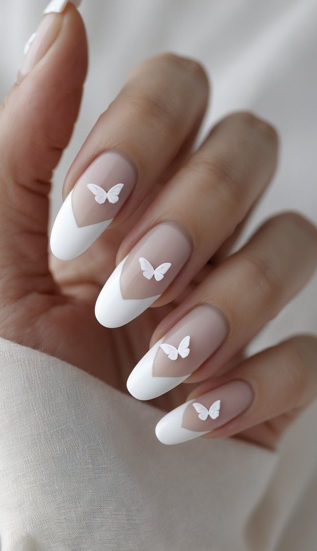 Hand with almond-shaped nails featuring a white French tip nail art idea with V-shaped tips and small butterfly decals on a nude matte base
