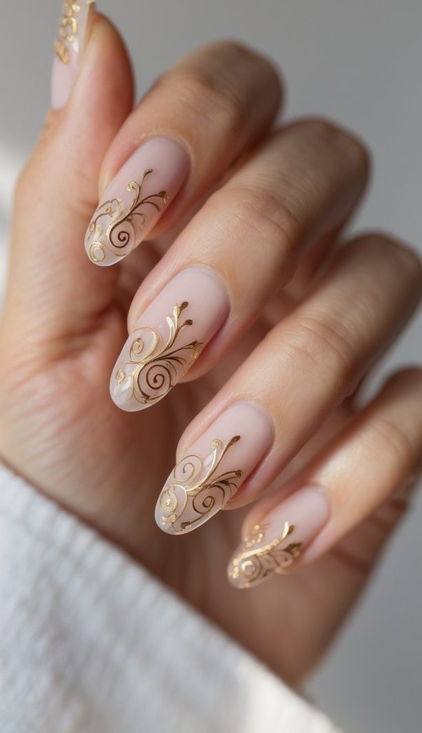 Almond nude nails decorated with fine gold details, presenting a sophisticated dainty nail art idea.