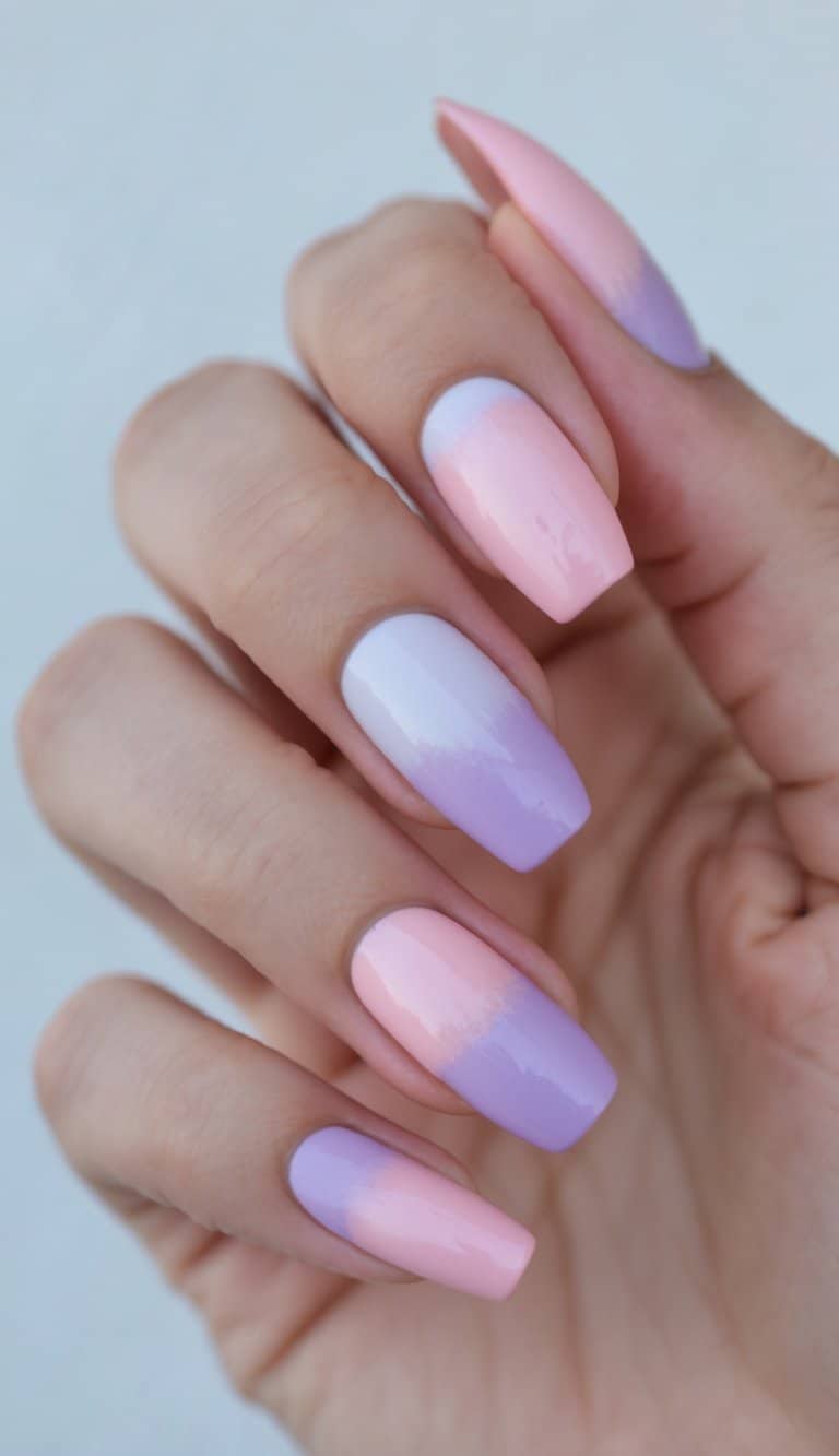 Photographed in soft light, a hand displays square-shaped nails featuring a gentle ombré shift from pale pink near the cuticle to lavender at the tips.