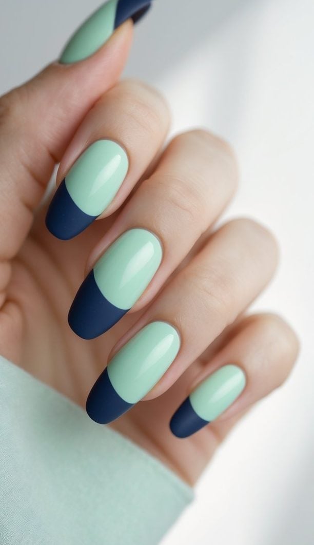 Photographed from a side angle, a hand displays almond nails in mint and navy shades, highlighting sharp tip detailing and a sleek two tone nail art idea.
