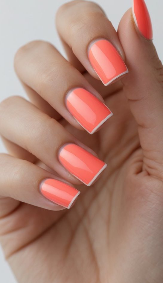 Detailed view of coral-orange manicure with fine white French edging, high-gloss polish, squared nail tips, and a modern colored French nail art idea look.