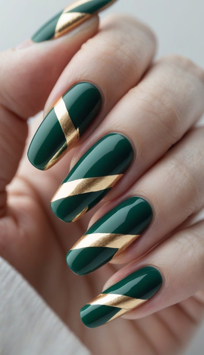 Long nails painted in glossy pine green, each accented with a perfectly diagonal gold band, showing a sleek green and gold nail art idea that plays on symmetry and shine.