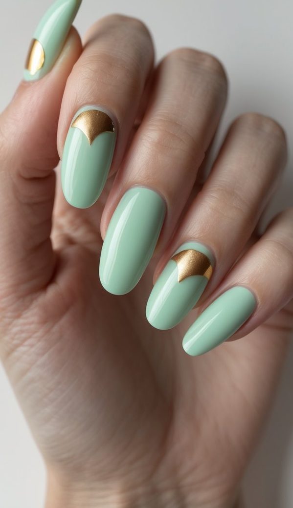 Close-up of manicured fingers with mint green nails and symmetrical golden cuticle accents shaped like crown arches, forming a chic green and gold nail art idea full of subtle glamour.