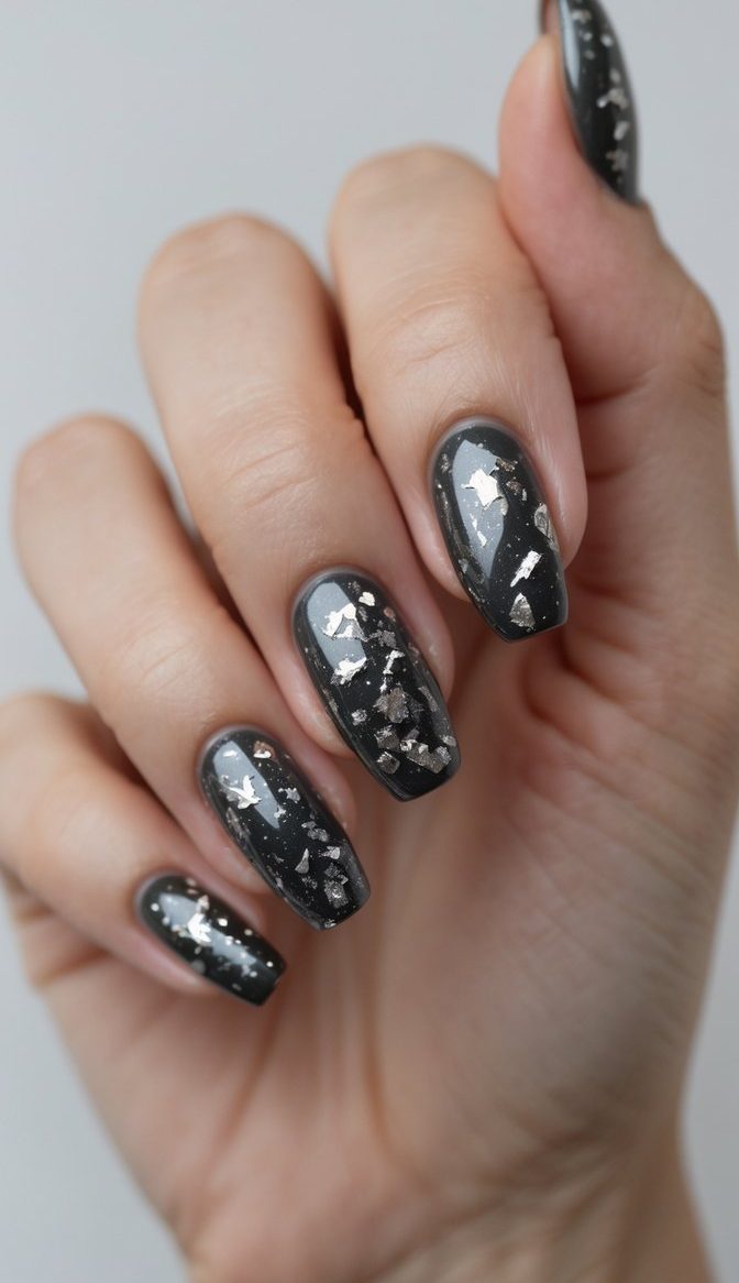 A close-up of a hand with charcoal gray nails featuring minimal silver foil specks, capturing a sleek and understated glossy nail art idea.