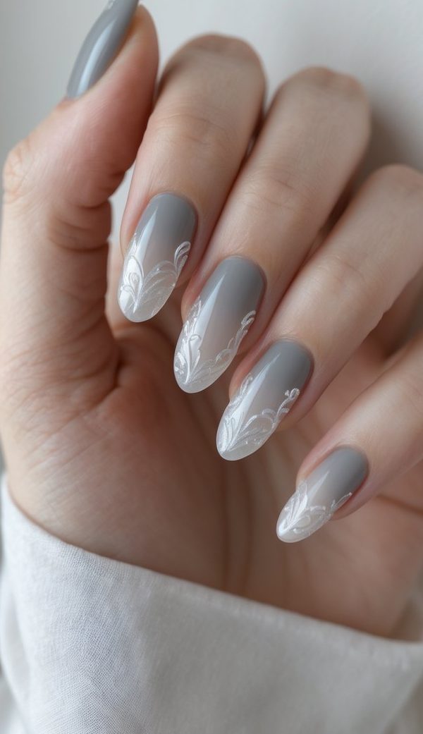 Pearlescent nail art idea on a hand with almond-shaped gray nails featuring soft white ombré tips and delicate leafy white detailing.