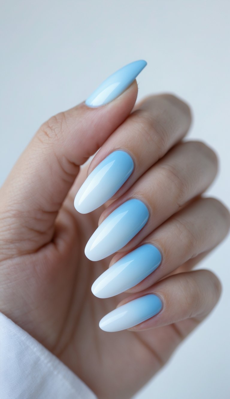 Hand with ombre French nail art idea showing a creamy transition from crisp white tips to pastel blue roots, on long shiny almond-shaped nails.