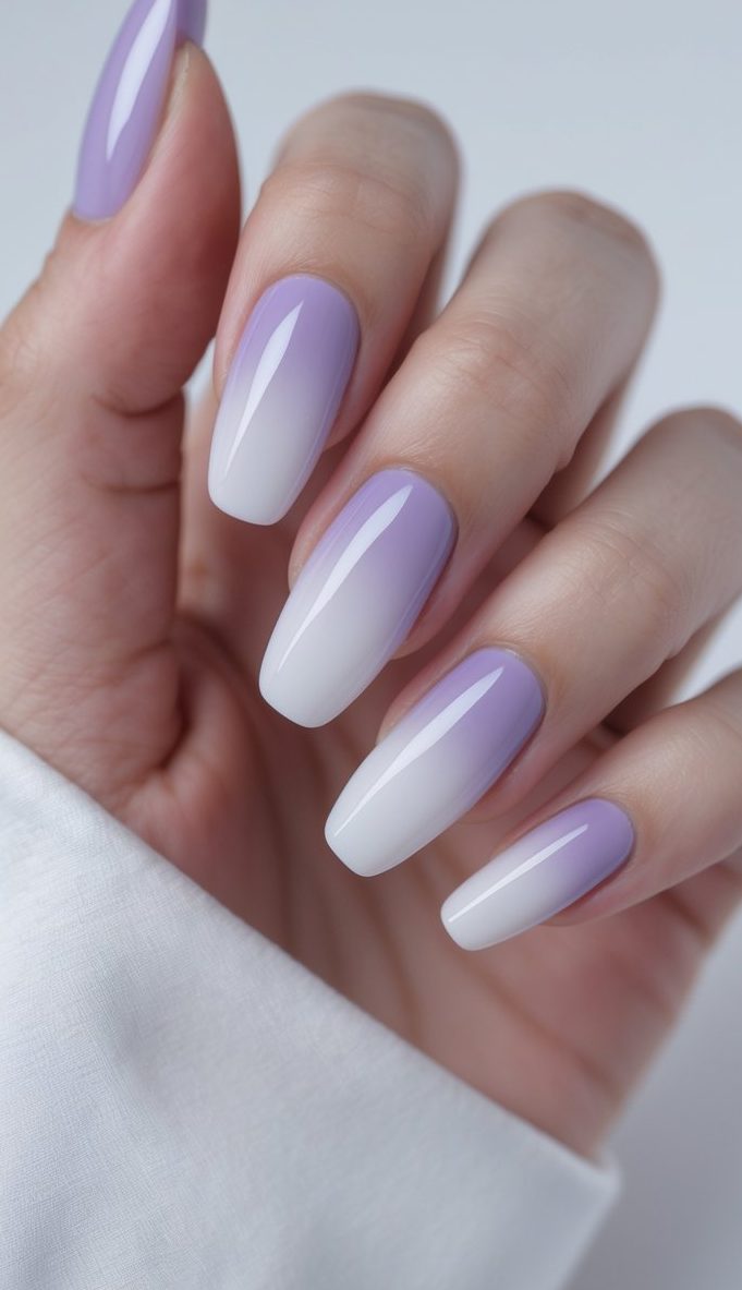 A hand with sleek ombre French nail art idea showcasing a smooth lilac-to-white fade on long, glossy nails against a minimalist background.