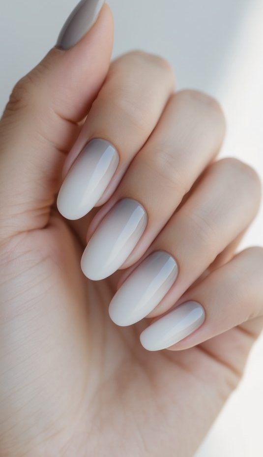 Close-up of a hand with almond nails painted in an ombre French nail art idea, featuring a subtle gray-to-white gradient in natural lighting.