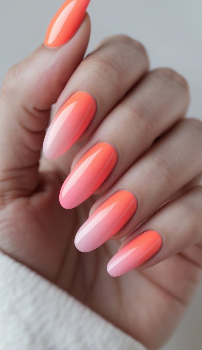 Close-up of one hand with coral to soft pink ombre French manicure on a white background.
