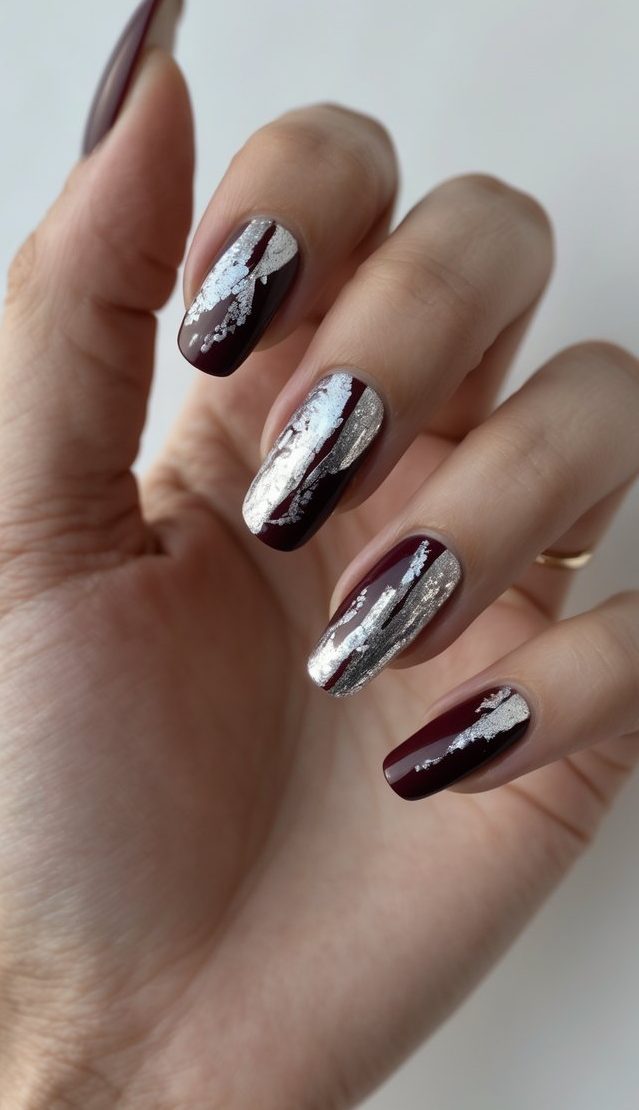 Nails painted with burgundy polish and irregular streaks of metallic silver foil, creating a foil nail art idea that looks electrified and dramatic.