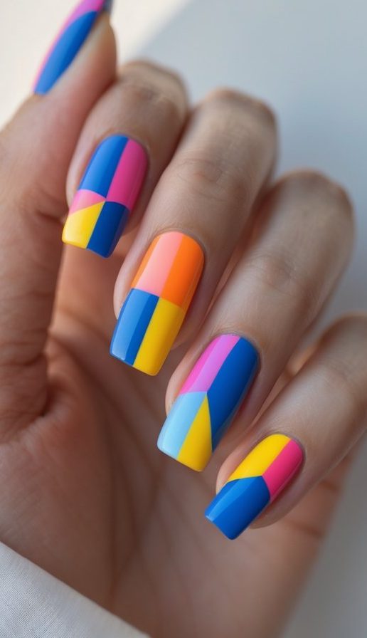Close-up of fingers painted with a colorful geometric nail art idea, showcasing abstract blocks of neon shades in a bright and playful palette.