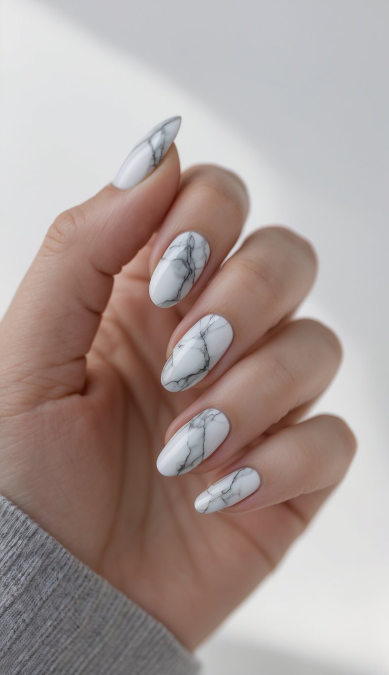 Neutral-toned hand with rounded almond nails painted in a marble nail art idea, featuring smooth white polish accented by thin grey marbled strokes