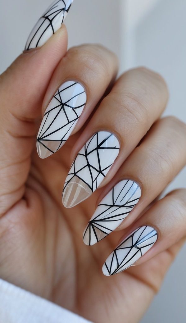 Almond nails on a slightly curled hand painted in sheer white and beige, decorated with fine black lines that form a fractured glass geometric nail art idea.