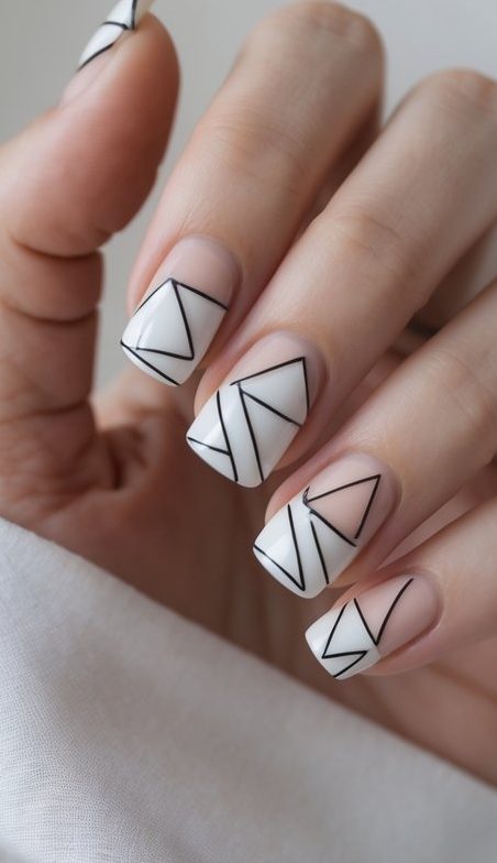 Fingers with square nude nails, each adorned with white triangle-shaped tips and sharp black linework, reflecting an origami-style geometric nail art idea.