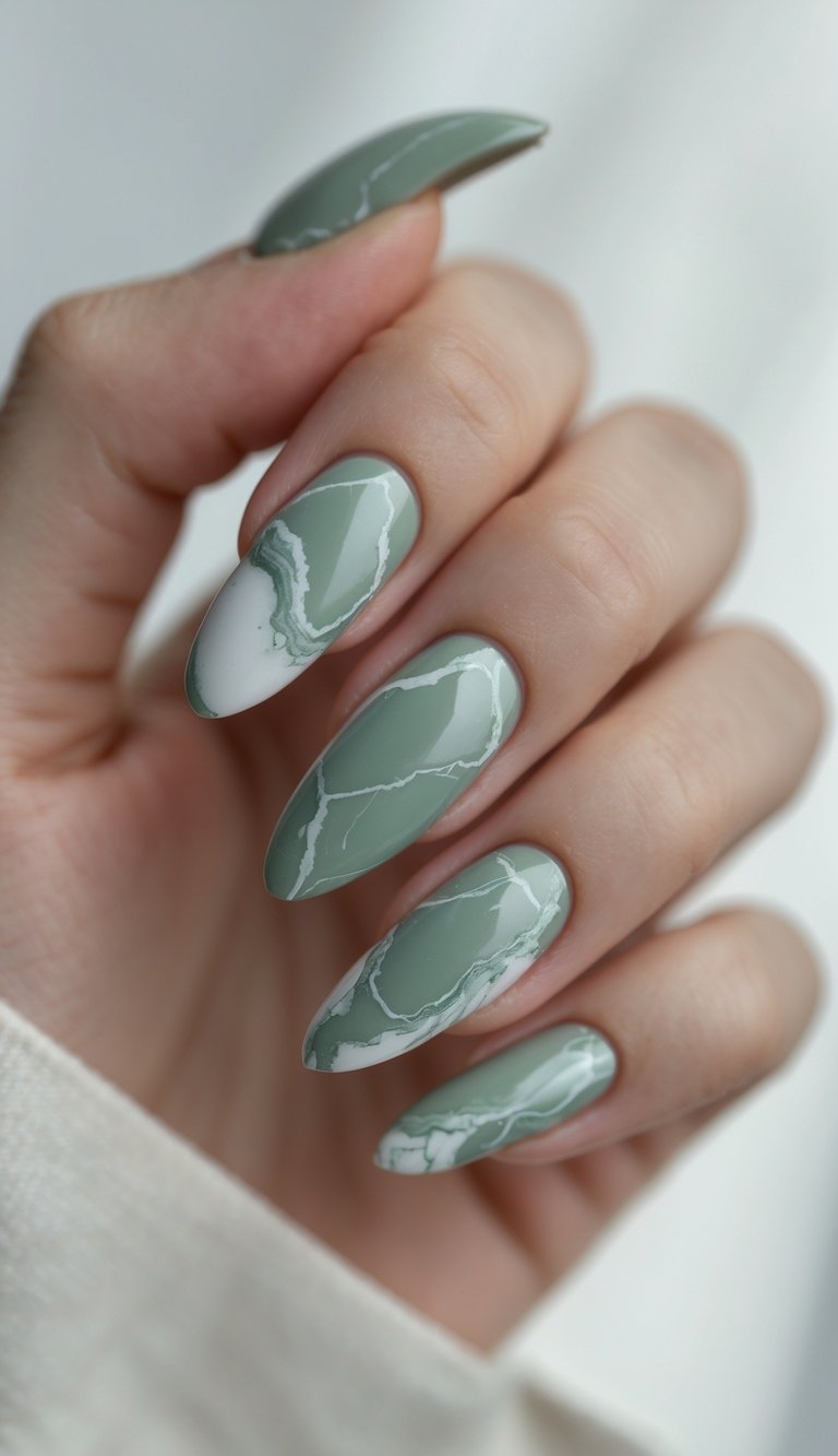 A close-cropped hand shows softly pointed nails glazed in dusty sage and traced with wispy white lines—an elegant marble nail art idea that blends calm and complexity