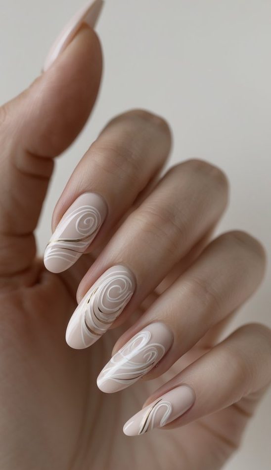 A graceful hand displays swirl nail art idea with nude polish, cream-white lines, and subtle metallic gold accents forming soft spiral waves.