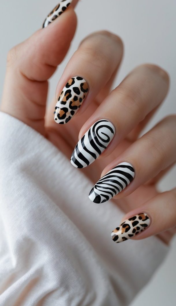 Editorial-style swirl nail art idea showing a hand with alternating zebra stripes, black swirl designs, and tan-and-black leopard print.