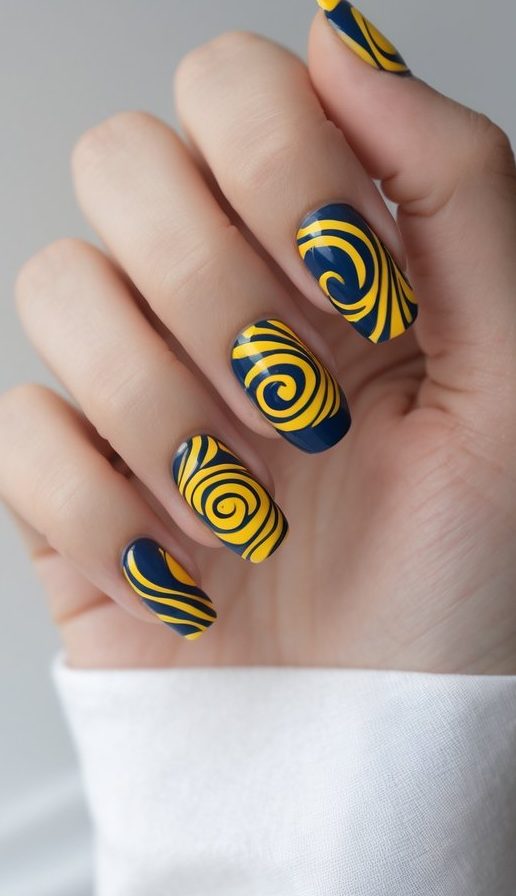 A close-up of a hand with artistic swirl nail art idea, using golden yellow spirals over a deep blue base to mimic a painterly finish.