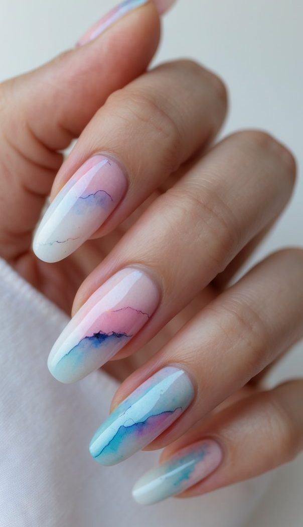 Delicate hand posed with nails fading from soft pink to seafoam, mimicking the cloudy layers of a painted sky—an airy watercolor nail art idea.