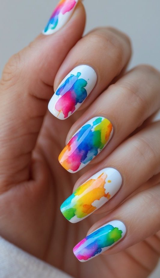 Fingertips painted with abstract rainbow splatters over a white base, resembling wet tie-dye—showcasing a bold watercolor nail art idea.