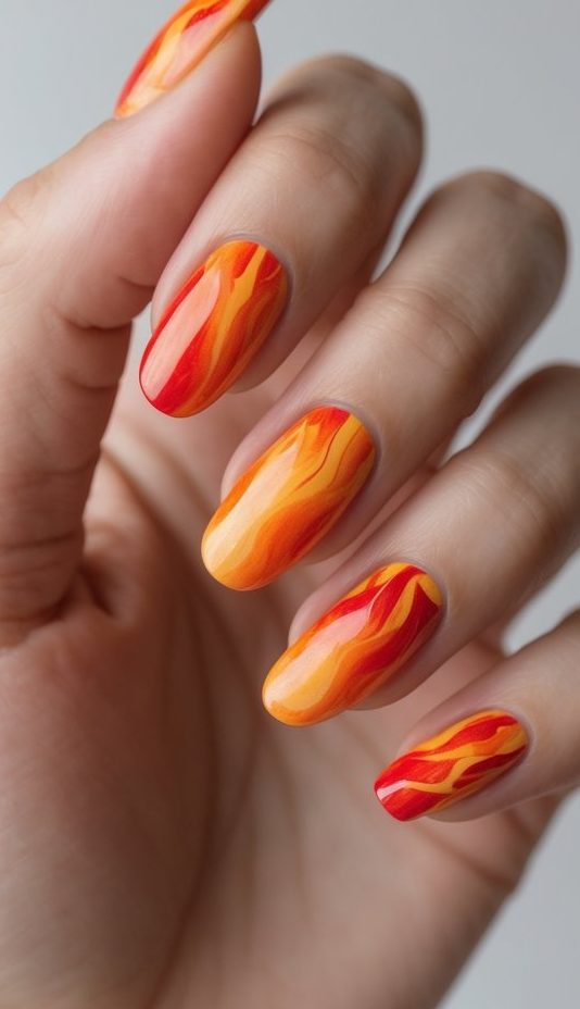 Close-up of glowing nails with sharp, flame-like strokes in red, yellow, and orange hues, blending fire and form into a dramatic watercolor nail art idea.