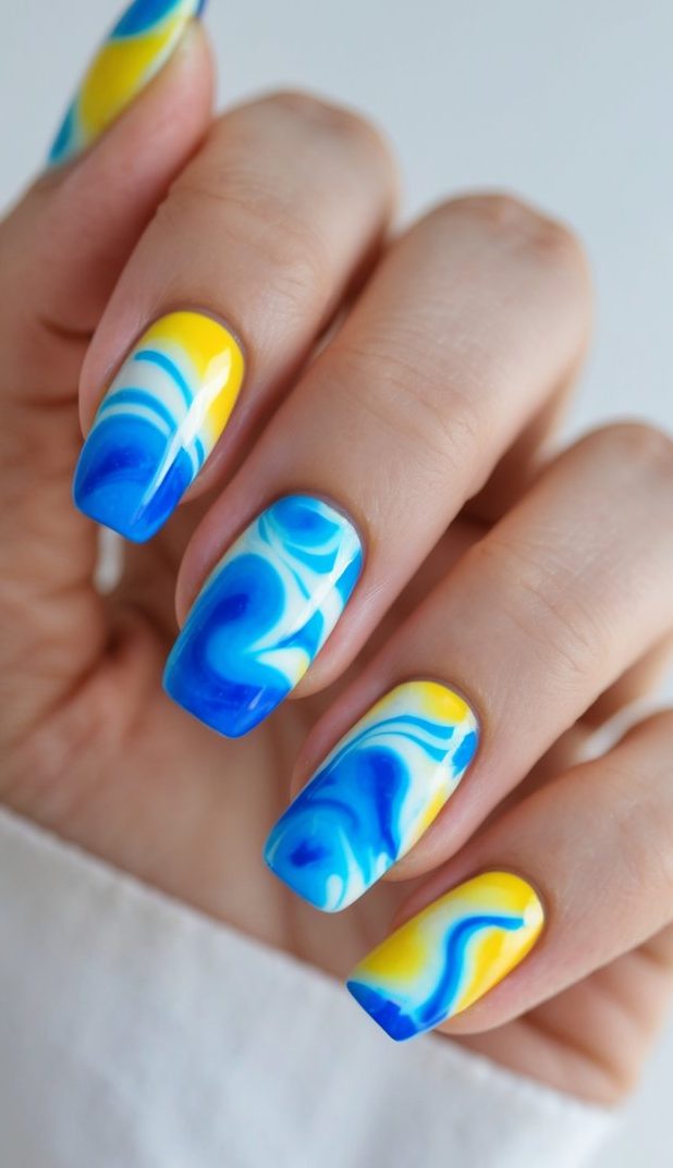A close-up of fingers flaunting square-shaped nails with a tie dye nail art idea in bold blue, white, and yellow swirl patterns.