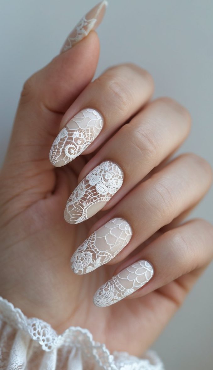 Elegant hand displaying a lace nail art idea with white floral lace patterns intricately painted on a nude almond-shaped nail base.