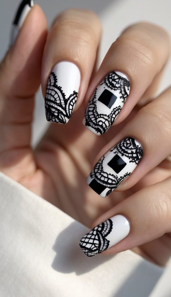 Close-up of a hand with an editorial lace nail art idea—white base polish adorned with geometric black squares and delicate black lace pattern overlays.