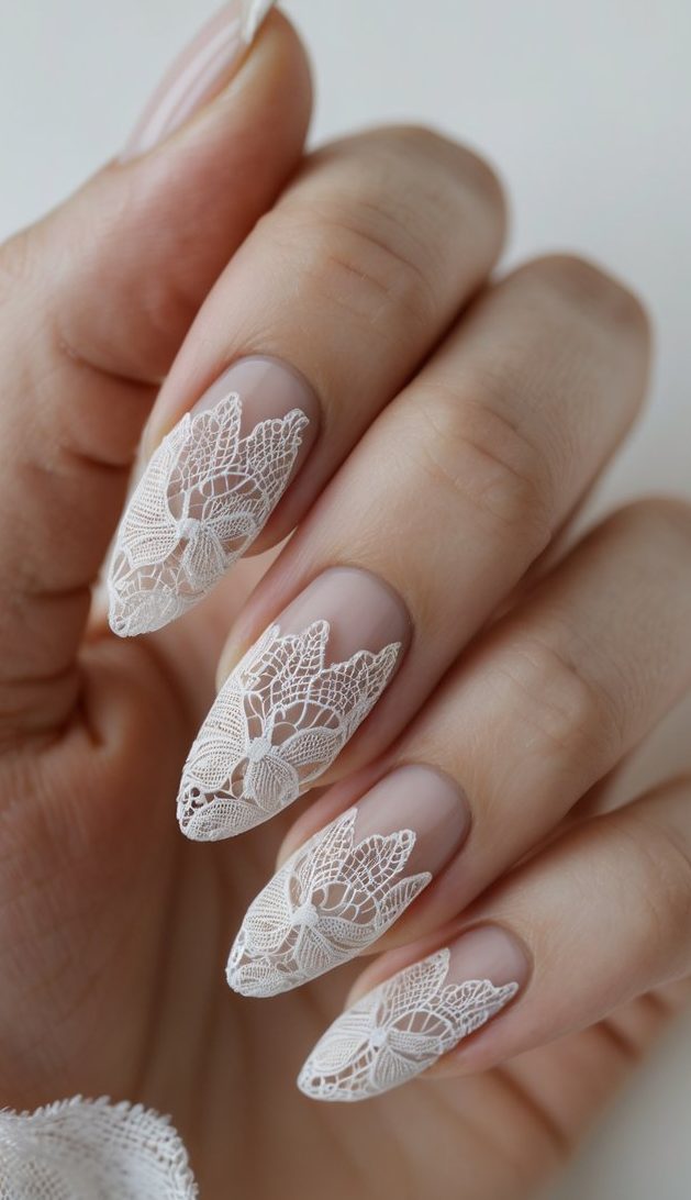 Hand with lace nail art idea showcasing pointed nude nails detailed with airy white lace in floral and leaf patterns, resembling bridal fabric.