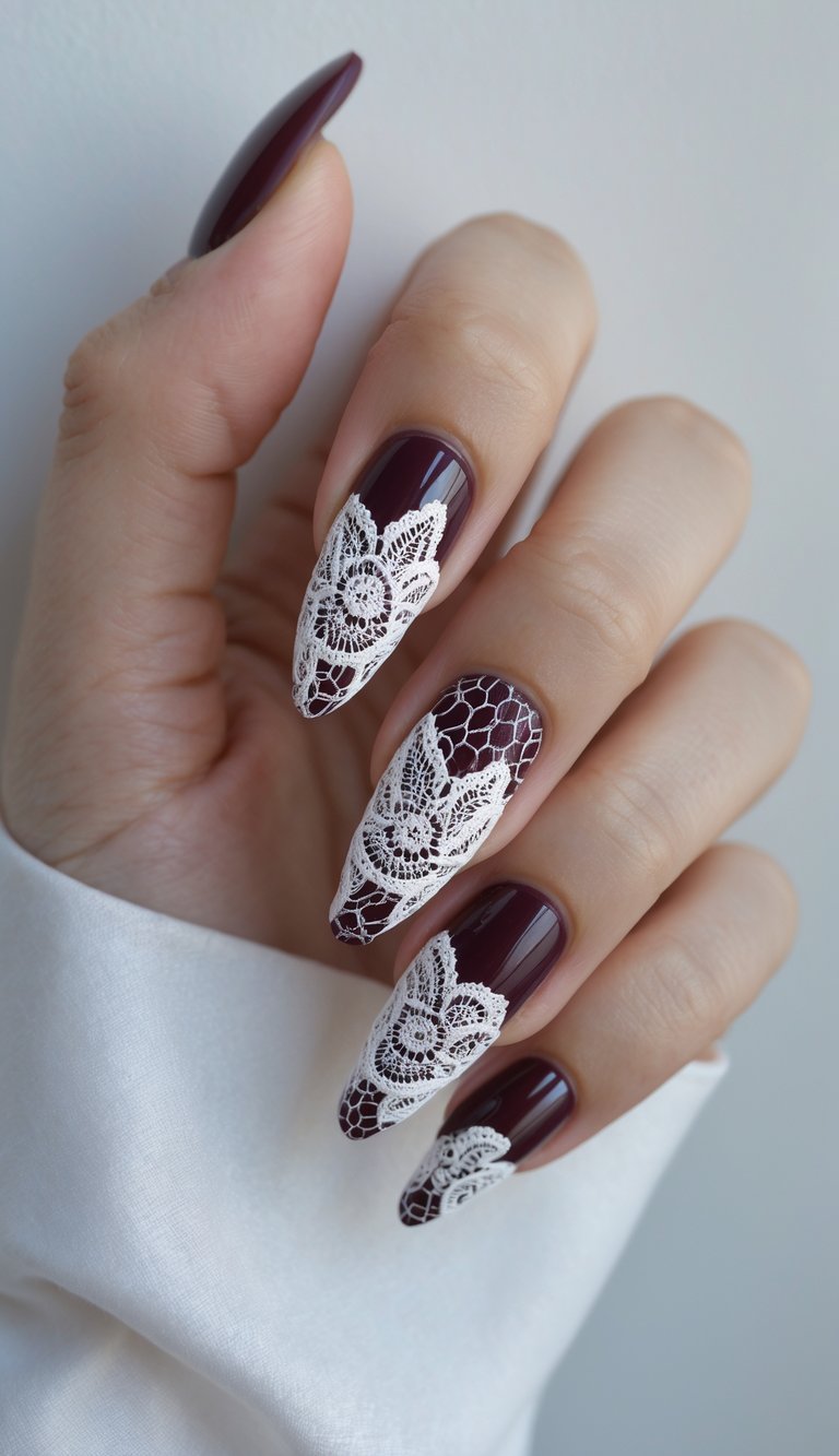 A hand displays a lace nail art idea on long burgundy nails with striking white lace florals and mesh patterns creating a vintage-meets-modern look.