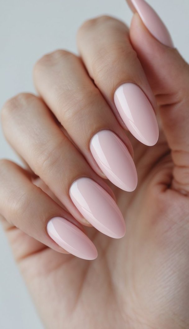 Natural hand showing elegant, glossy oval nails painted in sheer baby pink—an oval nail art idea with a subtle and sophisticated finish.