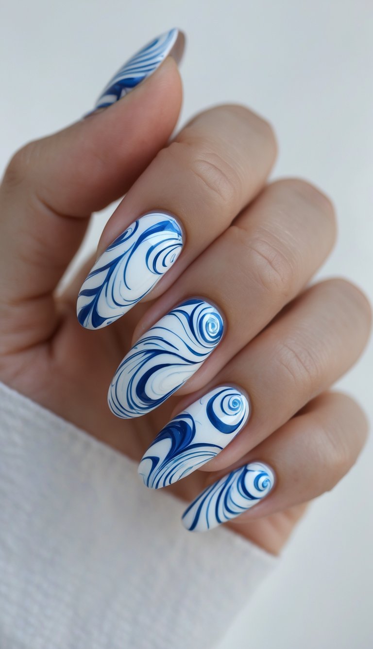 A hand with long oval nails featuring a bold mix of navy and cobalt blue swirls over a white background—an eye-catching oval nail art idea.