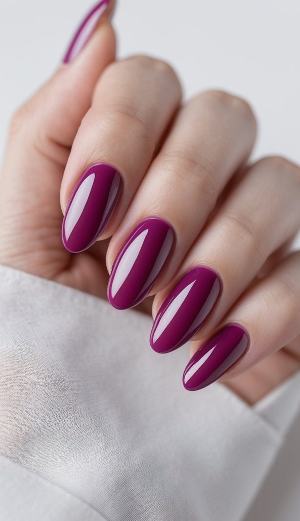 Close-up of hand featuring oval nail art idea with cabernet-colored nails finished in a bright, glossy topcoat and oval shaping.